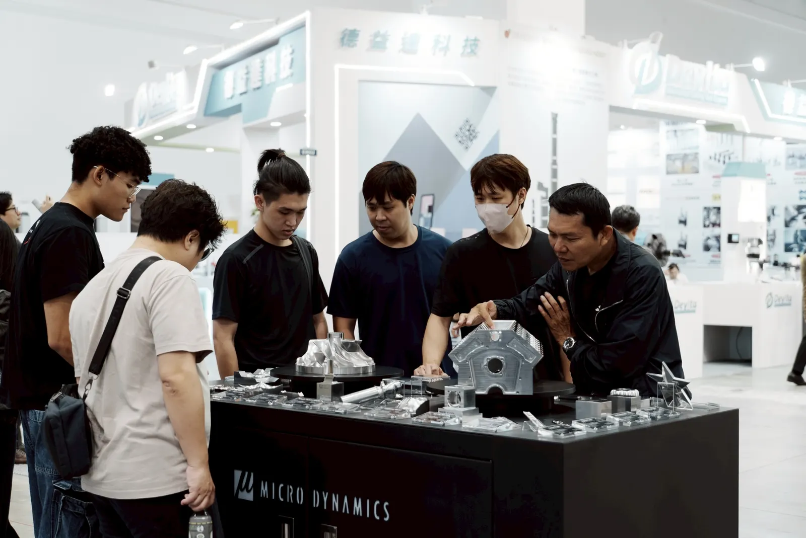 Booth visitors appreciating Micro Dynamics machined part accuracy, tight tolerances